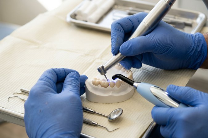 Close-up of gloved hands working on a tooth model with dental instruments